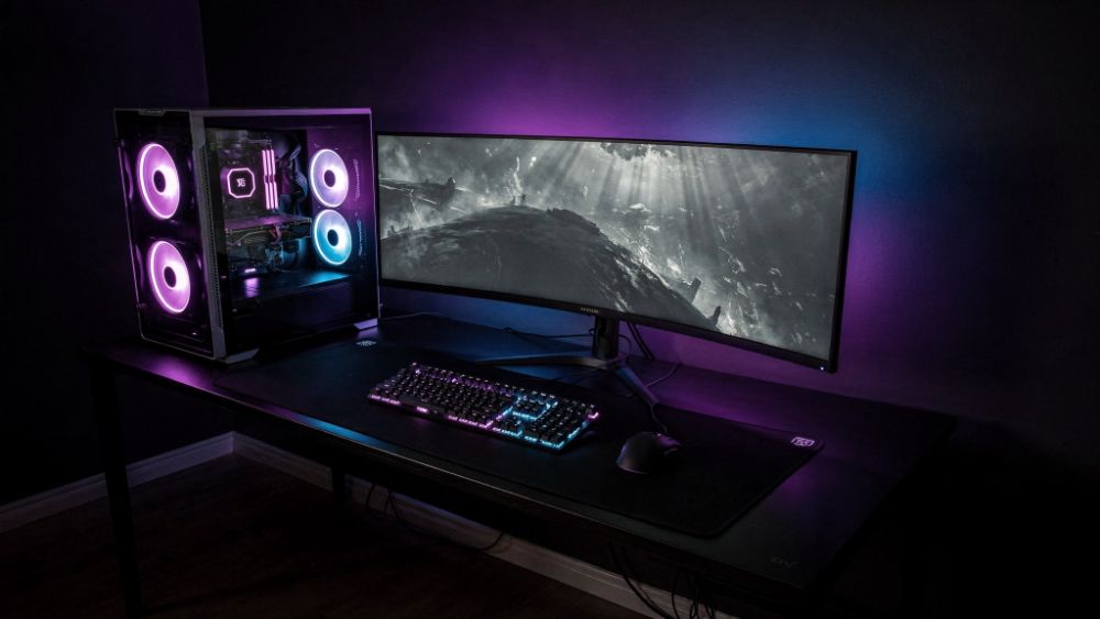 Setup gamer completo com torre, monitor e periféricos com iluminação RGB roxa e azul, estilo Nerdesk