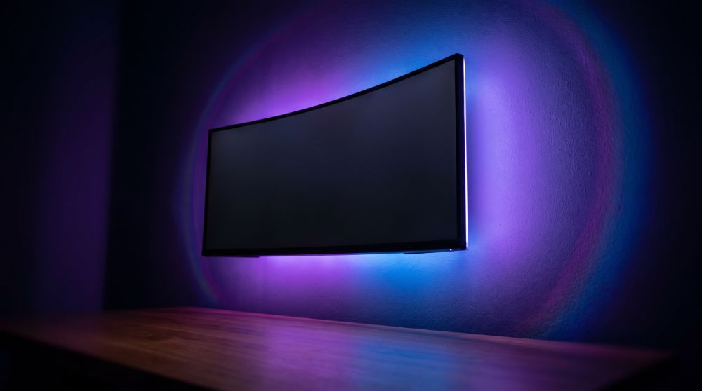 Iluminação RGB roxa e azul atrás de monitor curvo, estilo Nerdesk
