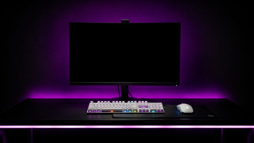 Estação gamer competitiva com teclado branco e iluminação RGB roxa e azul, estilo Nerdesk